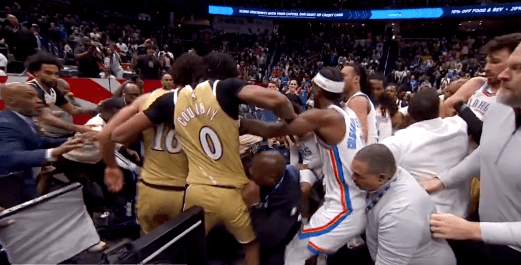 Basketball players in gold and white uniforms involved in a scuffle on the court.